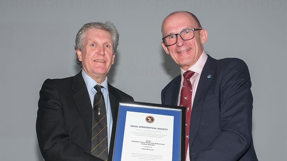 Anthony Buttler being awarded a certificate for the Fellow of the Royal Aeronautical Society. The two men are wearing suits and holding the certificate in the frame. They are smiling at the camera.